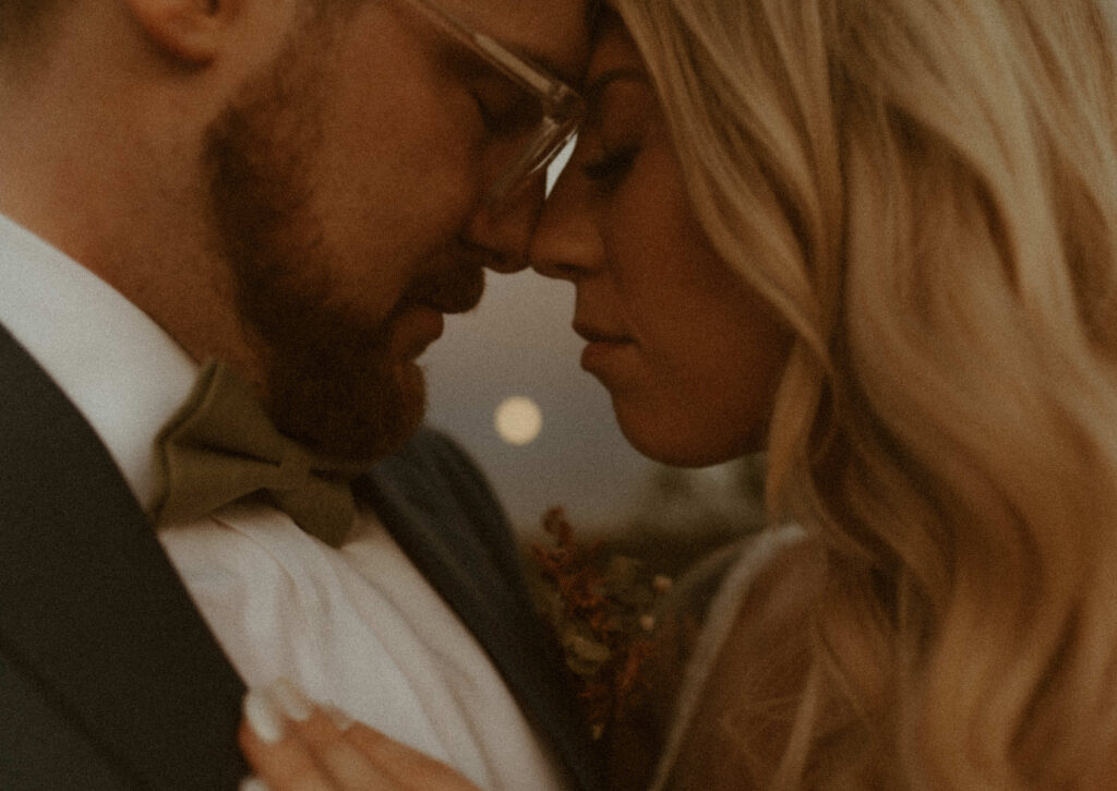 intimate close up of bride and groom with full moon in the background during their elopement at garden of the gods in colorado