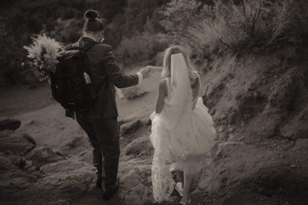 bride and groom walking holding hands with boho styled florals in backpack after their elopement