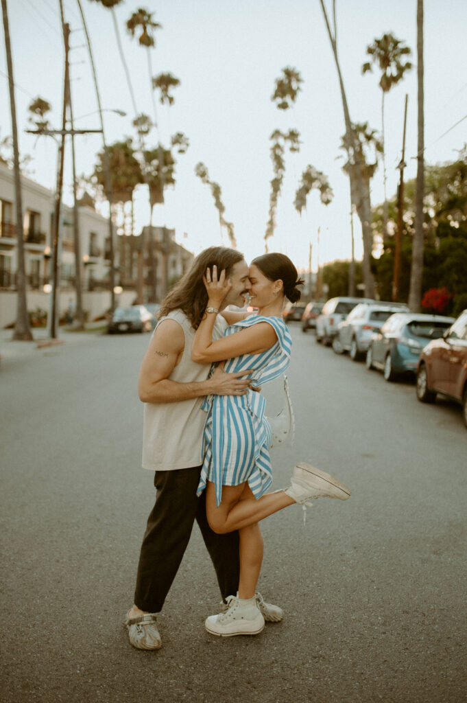 couple posing downtown Los Angeles on street with tall palm trees and cars in the background